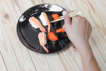 hand holding sushi chopsticks on a black plate wooden table  background