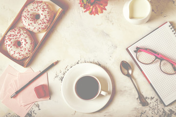 Notepad, donuts and coffee on white table.