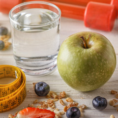 Healthy breakfast, dumbbells and measuring tape on wooden background.