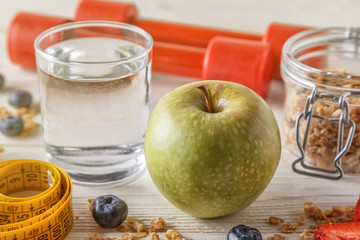 Healthy breakfast, dumbbells and measuring tape on wooden background.