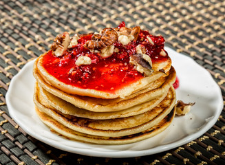 Homemade sweet pancakes with raspberry jam on a white plate. Breakfast with stack topped blueberry jam, walnuts and kiwi