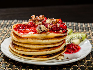 Homemade sweet pancakes with raspberry jam on a white plate. Breakfast with stack topped blueberry jam, walnuts and kiwi