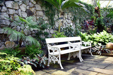 Obraz premium White bench placed beside a stone wall in the garden.