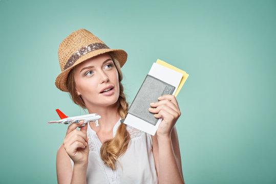 Closeup Portrait Of Beautiful Woman In Straw Hat Holding Airplane Model And Passport With Tickets Looking Away In Toughts At Blank Copy Space