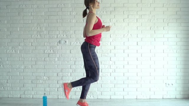 Young, pretty woman exercising, doing butt kicks at home, super slow motion
