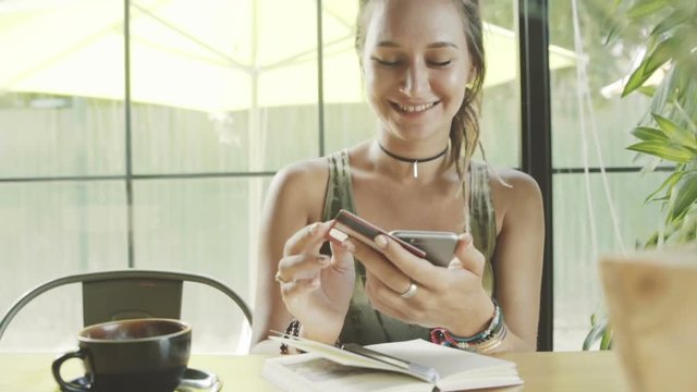 Woman using credit card shopping online with smartphone in cafe