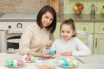 Happy mom and daughter painting Easter eggs