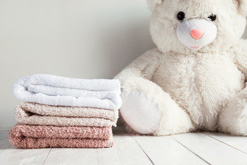Stack of spa towels on white wooden table with white soft toy bear on background. Childrens washing...