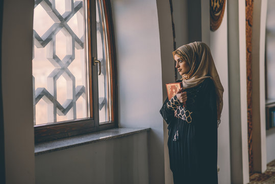 Beautiful Muslim girl standing next to a window