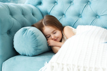 Dreamy little girl sleeps under white blanket on blue couch