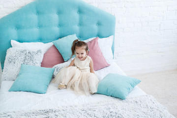 Laughing little child sits among blue and pink pillows on bed