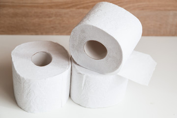 Rolls of white toilet paper on white and wooden background.