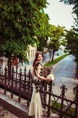 Girl in fancy dress poses on stone bridge with steel handrails