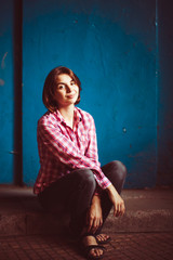 Thoughtful lady in jeans and plaid shirt sits before blue wall