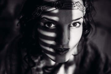 Black and white picture of stunning woman with wreath on her forehead and rays of sun on her cheeks