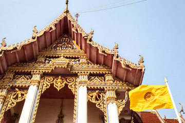 Traditional golden Thai Buddhist temple with carved ornaments and yellow Buddhist flag. Asian religious landmark against the sky. Wat Chaimongkhon Royal Monastery in Pattaya, Thailand