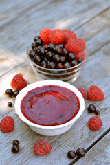 Vitaminic, red jam of home blackcurrant and red raspberry in white plate neat glass plate with full berries on wooden texture close up 