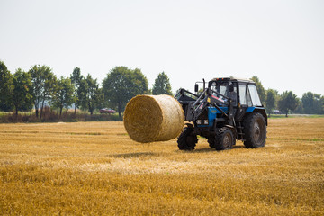 Vinnitsa,Ukraine - July 26,2016.huge tractor collecting haystack in the field at nice blue sunny...
