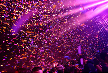 Confetti fired on air during a concert. People are happy and with hands in the air. Image ideal for backgrounds. Pink and purple are the tones of the picture