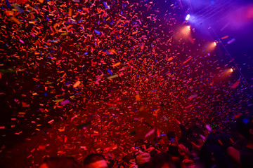 Confetti fired on air during a concert. People are happy and with hands in the air. Image ideal for backgrounds. Red is the tone of the picture