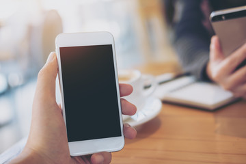 Mockup image of businessman and businesswoman's hands holding and using smart phone on wooden table