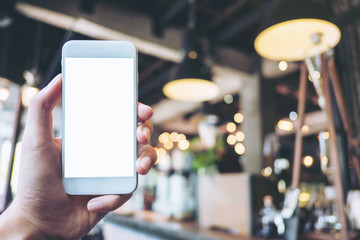 Mockup image of a hand holding white mobile phone with blank white screen in vintage loft cafe