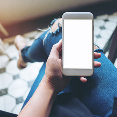 Mockup image of hand holding white mobile phone with blank white screen on leg with a vintage tile floor in cafe , feeling relax