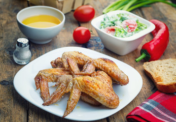 .Roasted chicken wings, salad, salt, vegetable oil, red pepper, tomatoes, chives and bread on a rustic wooden table. Focus concept.