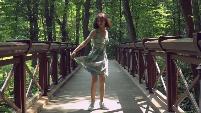 An attractive lady is whirling in the forest and bends her back across the wooden bridge afterwards. Her spring colored dress is waved during the spins.