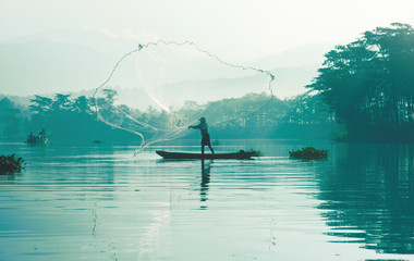 Fisherman casting out his fishing net in the river by throwing it high up into the air early in the...