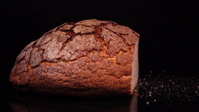 Fresh baked cut round bread with crumbs rotating against black background. Close up view. Tasty pastry product for your breakfast in 4K Ultra HD 3840x2160
