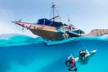  A freediver swims underwater next to a traditional boat on a tropical coral reef © whitcomberd