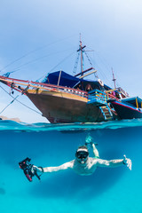 Snorkeller freedives below the surface in front of a traditional wooden boat © whitcomberd