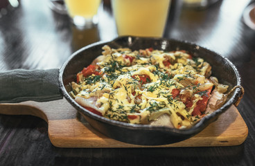 Frying pan with meat, vegetables and potatoes under melted cheese with golden beer