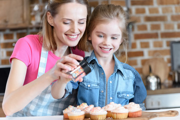 portrait of smiling daughter and mother decorating cupcakes