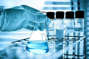Flask in scientist hand with test tubes in laboratory  