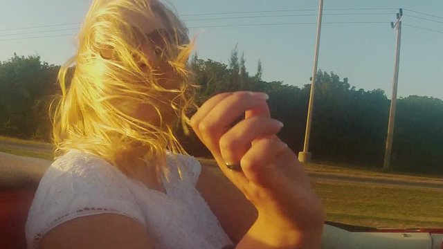 Young blonde woman riding in a convertible car at the evening