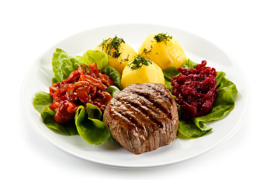 Grilled steaks, boiled potatoes and vegetable salad on white background