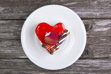 The dish is white with cake in shape of heart on wooden background