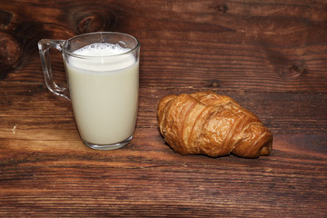 The morning breakfast of milk and croissant on a wooden table.