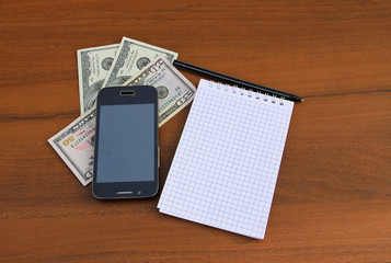 Notepad with pen, smartphone and dollar cash on wooden desk