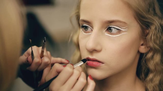 Make-up artist makes young actress girl beautiful makeup for lips before dancing perfomance indoors