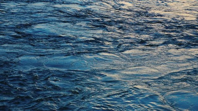 Dark blue water surface with moving ripple and air bubbles, slow motion.