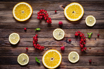 Lemon and orange rings, red currants, raspberries and mint leaves on wooden background. Table top view. Fresh fruit composition / layout.