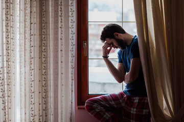 Young sad mad sitting by the window in regret