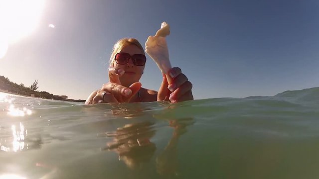 Young blonde woman in a sea with seashell in hands