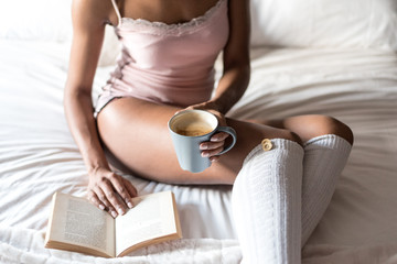 woman reading a book and drinking coffee on bed with socks