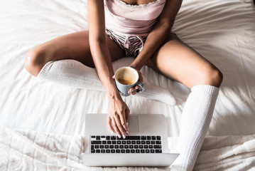 woman on bed drinking a coffee and working with her computer