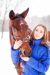 Fototapeta premium Teenage girl feeding bay horse on winter field. Friendship concept image