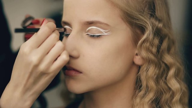Make-up artist makes young actress girl beautiful makeup for eyes before dancing perfomance indoors